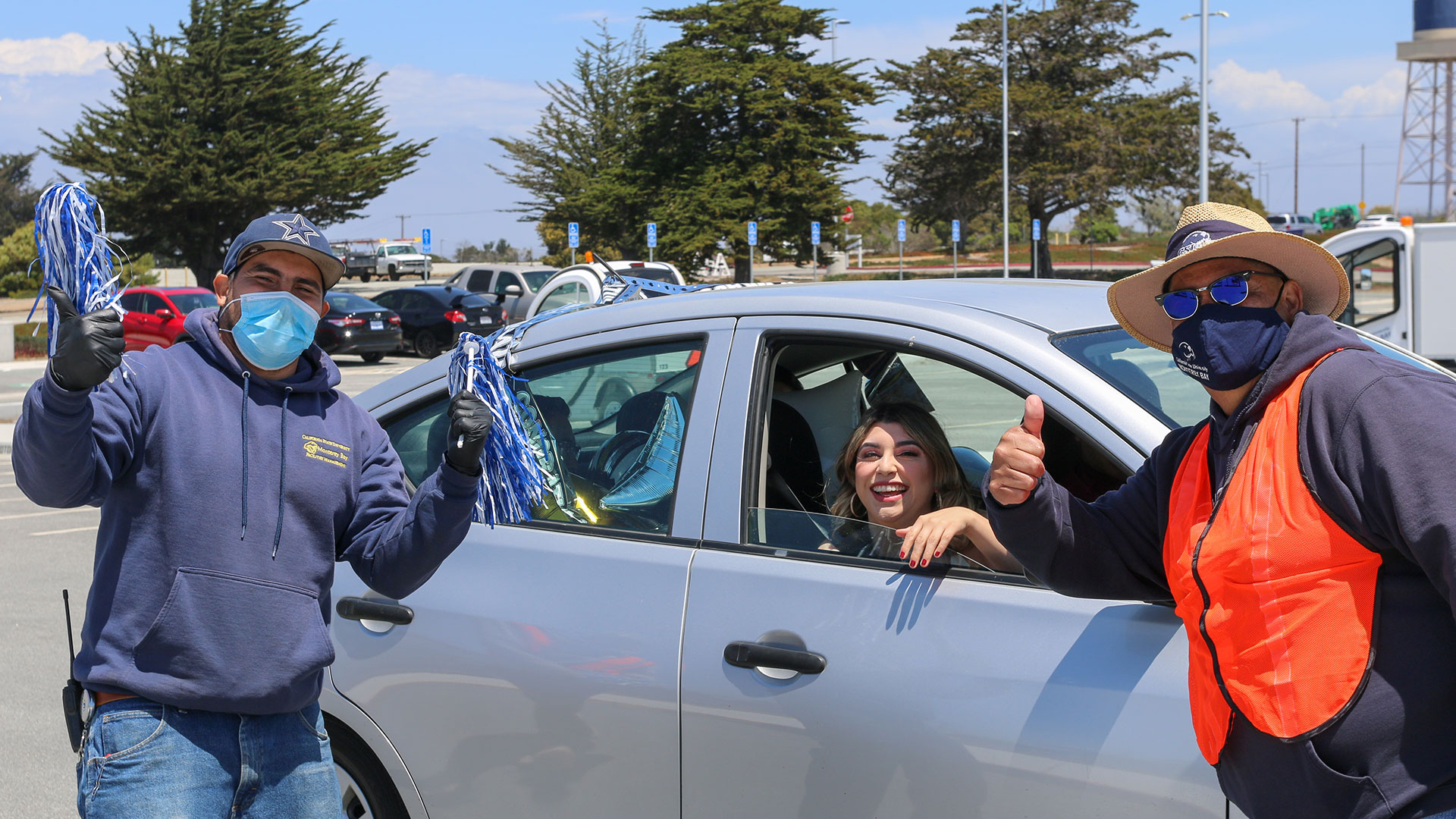 Graduate in car, smiling with staff members