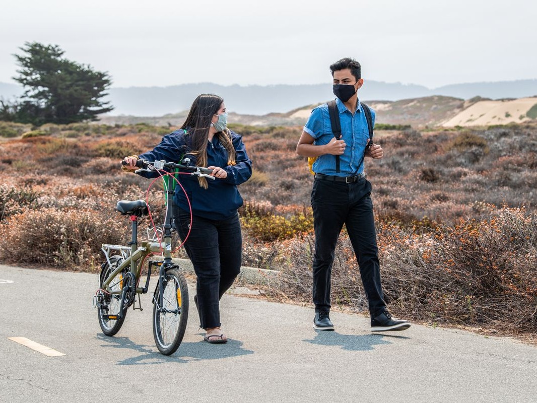 A female student walking her bike down the road with a male student