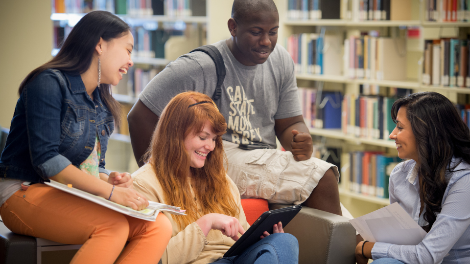 Students in library looking at ipad and laughing