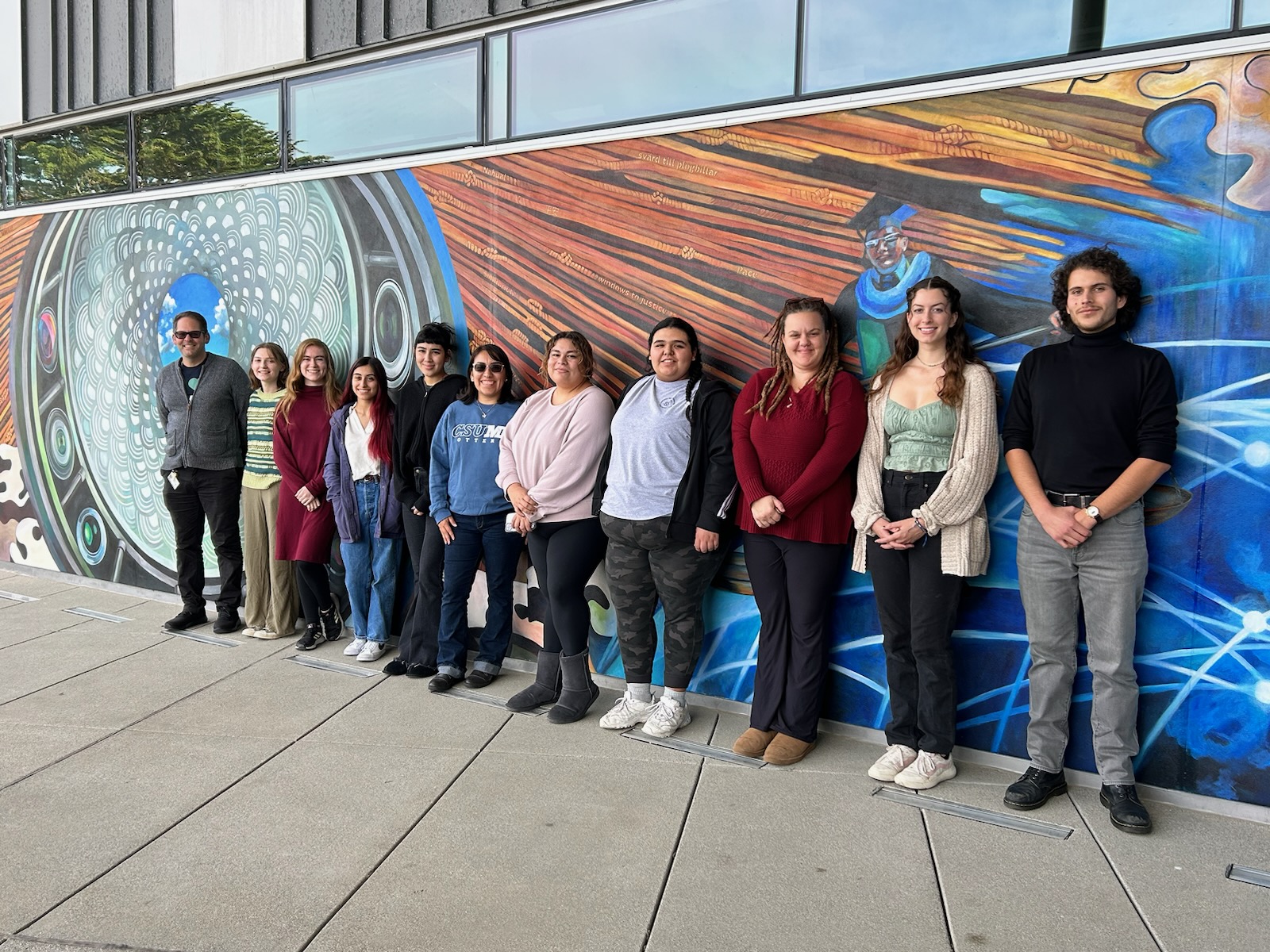 Student award winners shown lining up in front of a mural