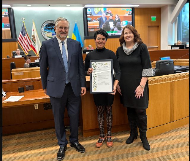 rachelle is flanked by a man and woman holding certificate