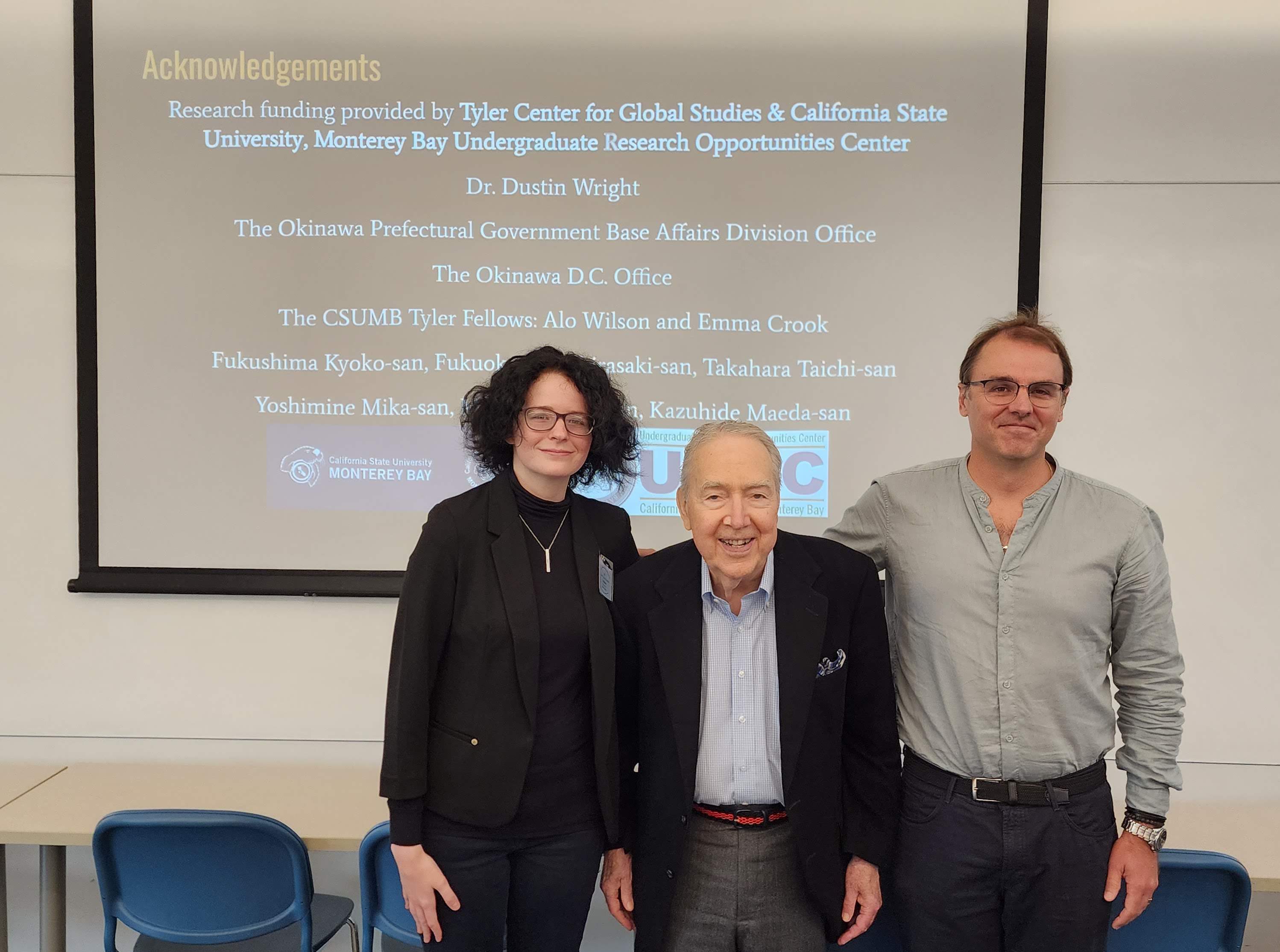 3 individuals pose in front of classroom projector screen