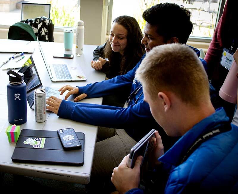 Three people looking at a laptop during Hackathon