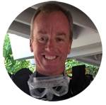 James smiling while taking a selfie. He's wearing a diver's wetsuit and goggles; the goggles are on his neck.