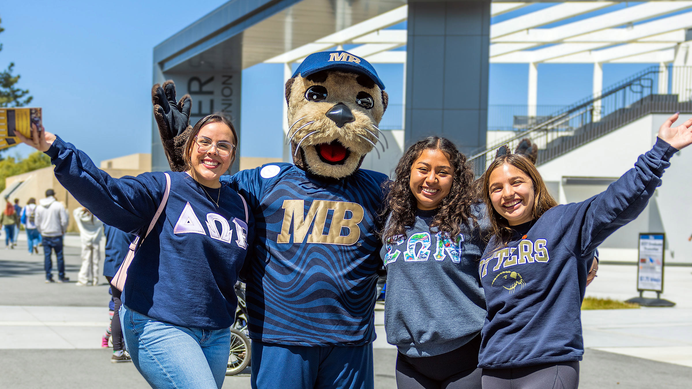 Three students and Monte with their arms around each other on Admitted Otter Day.