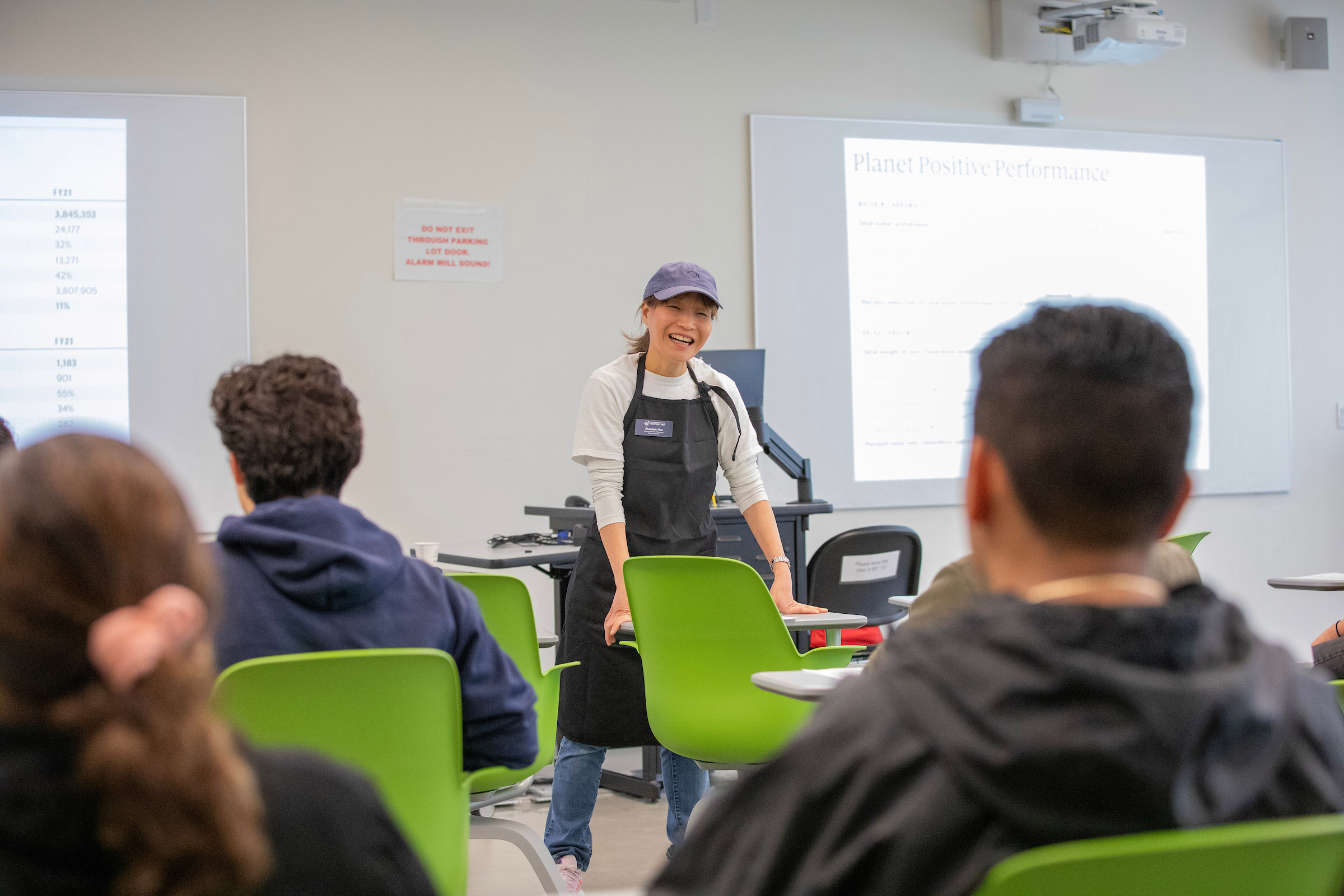 A professor leans over a green chair and smiles to a group of students on Admitted Otter Day.